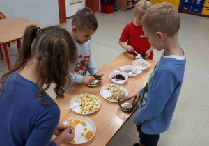 Dzieci wkładają do miseczek z jogurtem musli i owoce